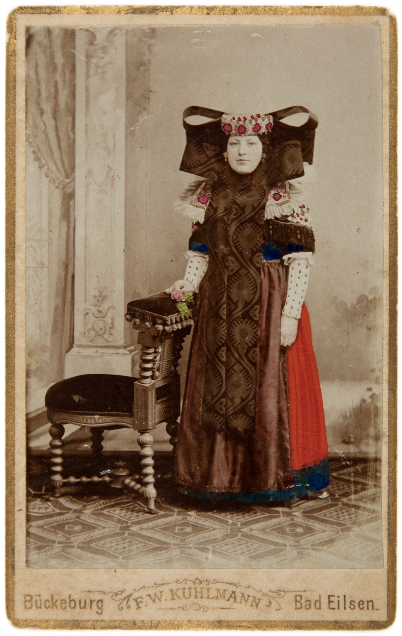 Handkoloriertes Porträt einer Frau in Bückeburger Tracht neben einem Stuhl, Atelier F. W. Kuhlmann in Bückeburg und Bad Eilsen